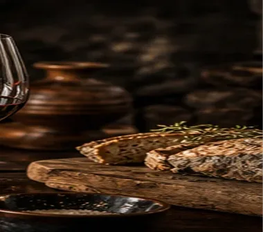 A board of wood-oven bread with fresh thyme, a clay jug and a glass of red wine on the counter
