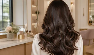 Long, softly waved brunette hair from behind, in a warm styling room