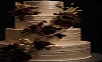 A tiered white wedding cake with burgundy blooms