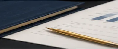 A navy leather notebook, gold pen, and printed charts on a desk